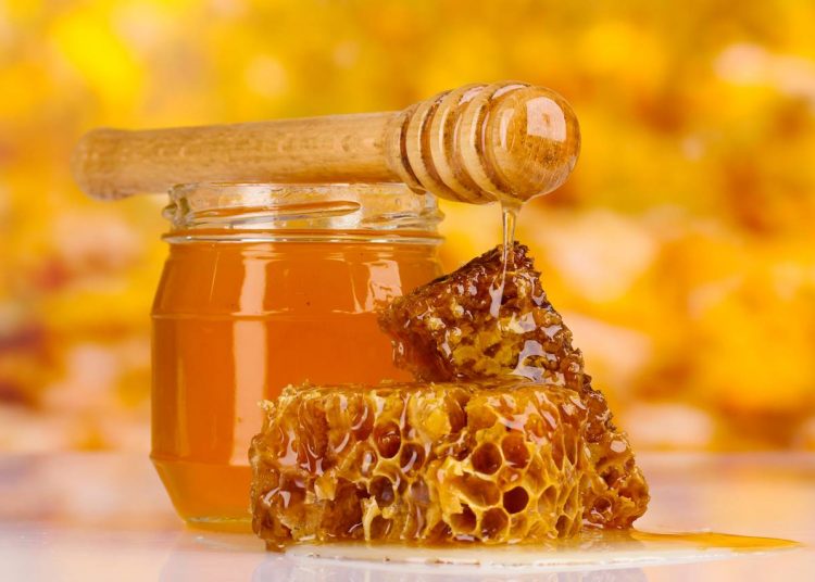 jar of honey, honeycombs and wooden drizzler on yellow background